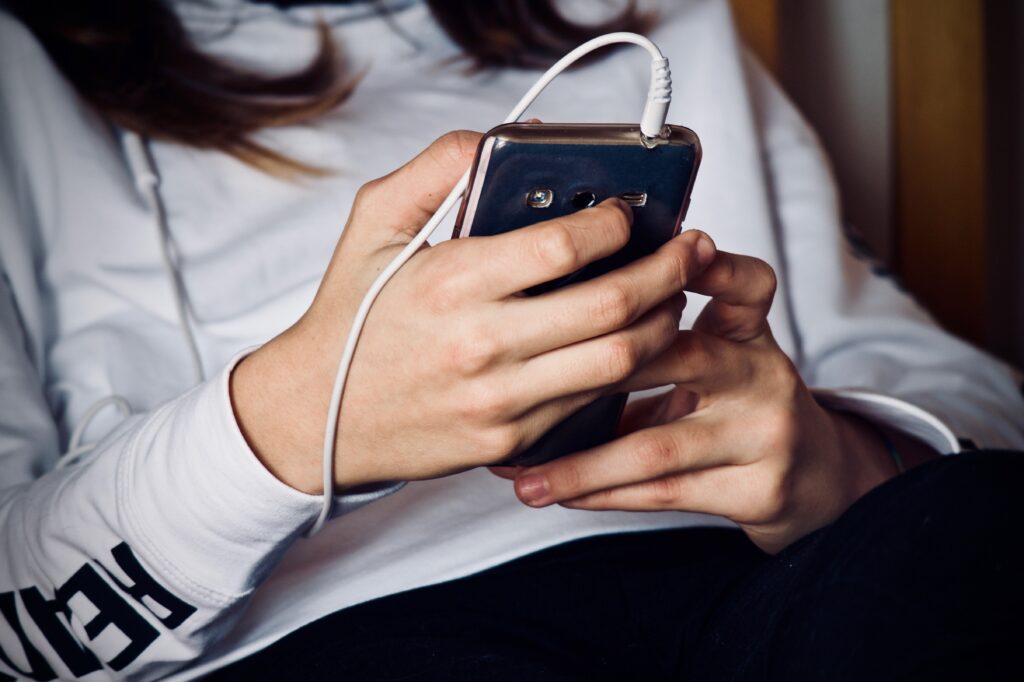 Pessoa usando celular com fones de ouvido, representando atenção aos golpes digitais e links suspeitos.