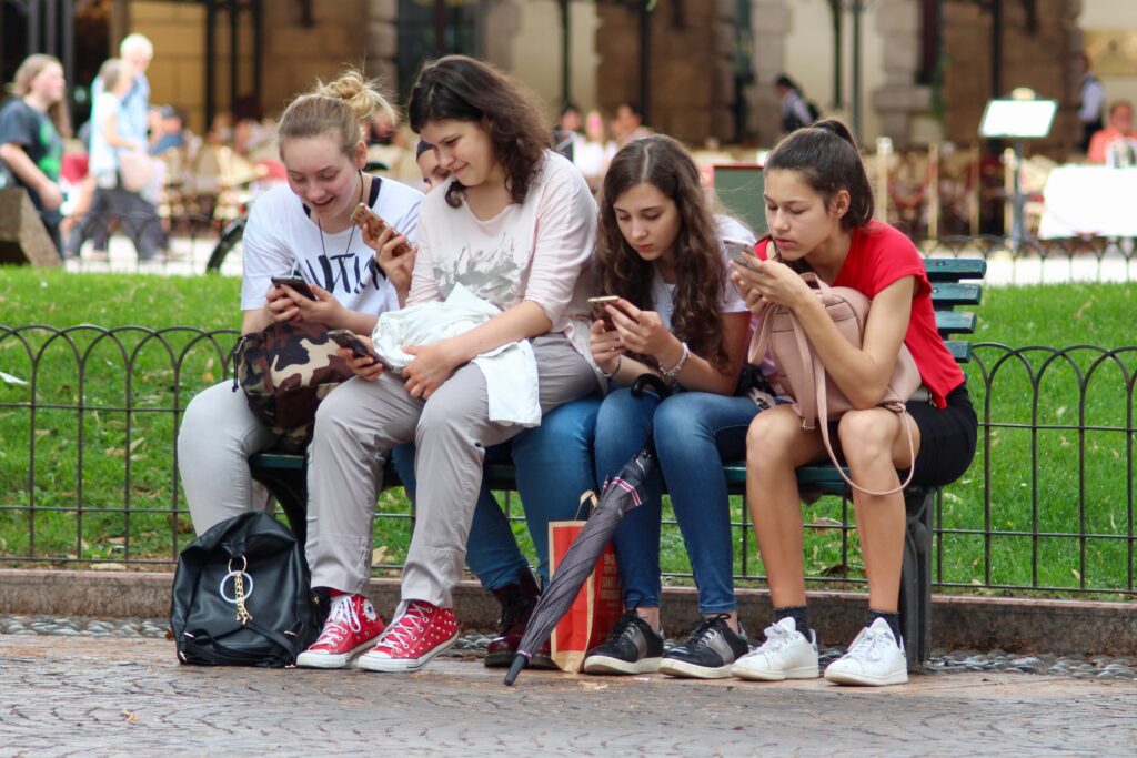 Grupo de jovens usando celulares em um banco ao ar livre, representando a importância da segurança online para proteger a família.