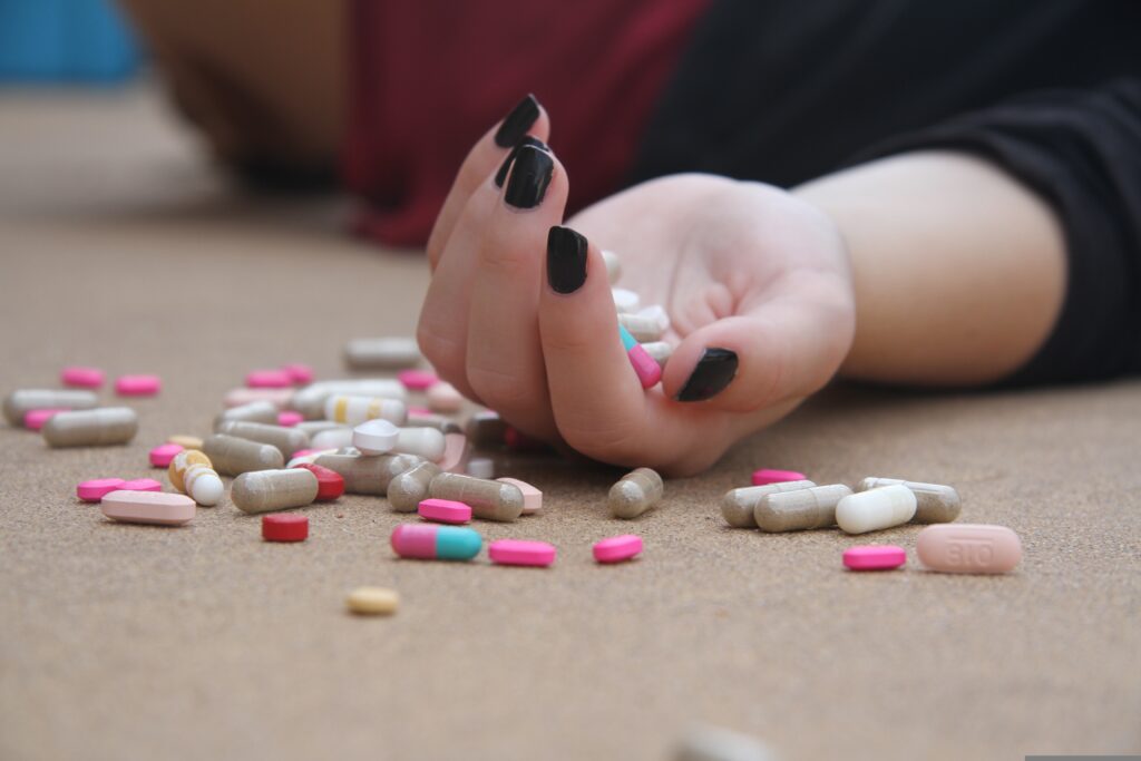 Mão de pessoa caída ao lado de comprimidos, representando crise emocional e alerta para saúde mental no trabalho