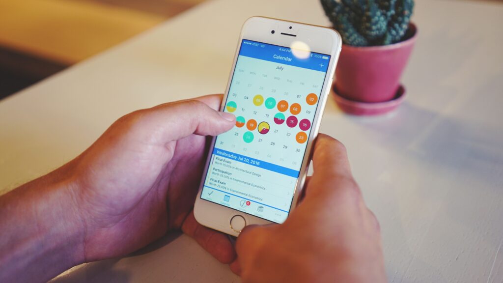 Pessoa segurando um celular com calendário aberto, representando planejamento de postagens médicas nas redes sociais.